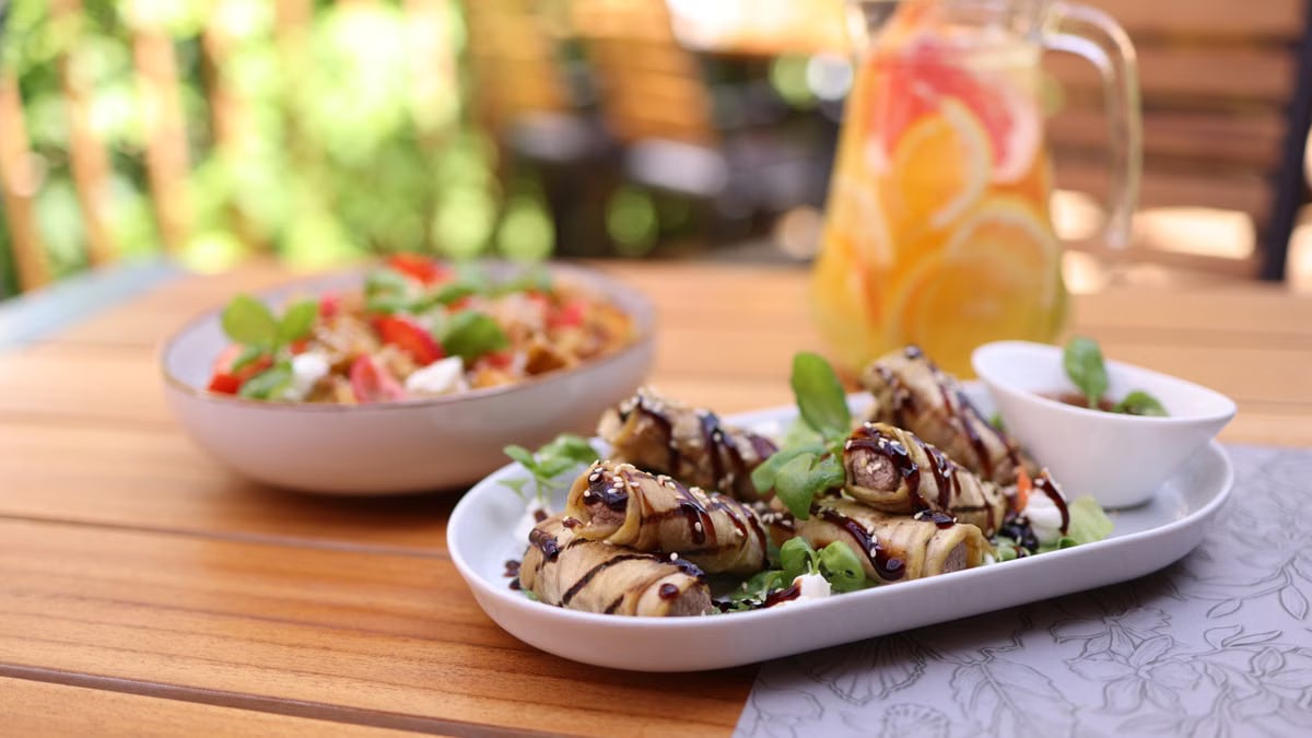 Delicious outdoor brunch with eggplant rolls, salad, and citrus juice on a sunny day.